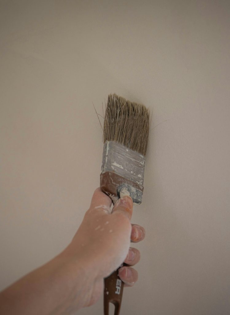 A hand painting an interior wall with a large brush, emphasizing DIY home improvement.