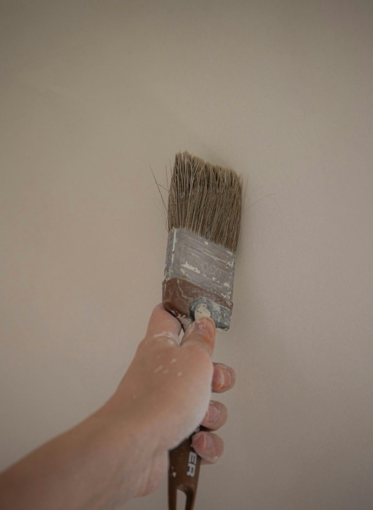 A hand painting an interior wall with a large brush, emphasizing DIY home improvement.